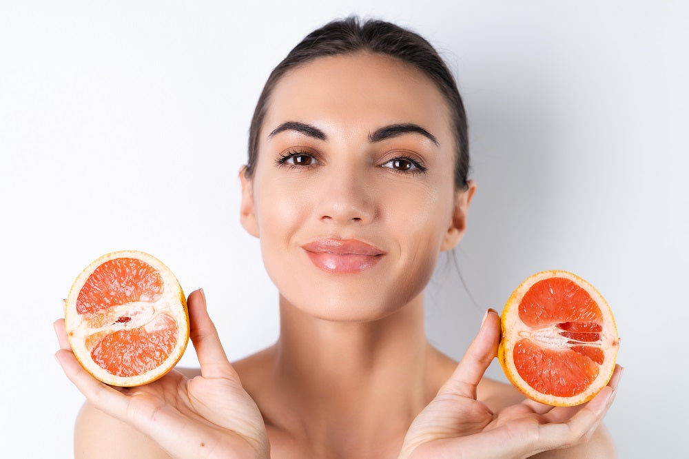 Close-up portrait of topless woman with perfect skin and natural make-up, full nude lips, holding fresh citrus vitamin C grapefruit